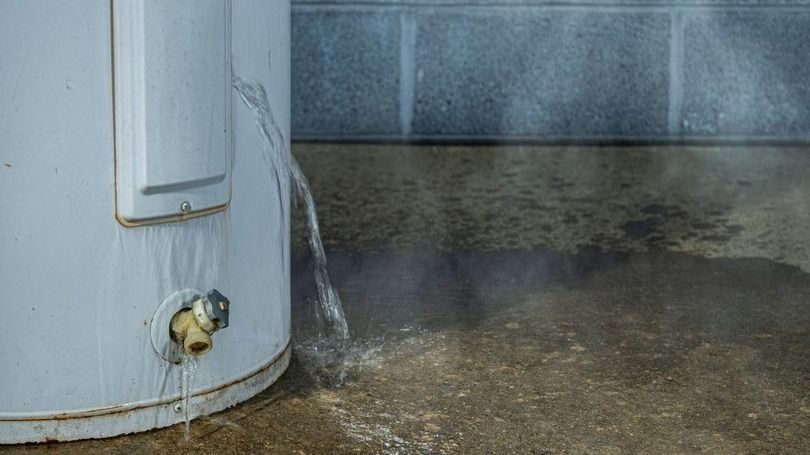 Water heater with a leaky valve dripping water onto a wet concrete floor, creating steam.