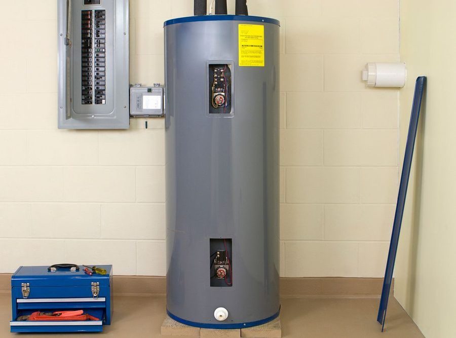 Vertical grey water heater in a utility room with an electrical panel, toolbox, and a long blue pipe leaning against the wall.